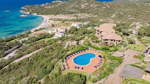 An aerial view of a coastal resort with a swimming pool, multiple villas, and a beach.