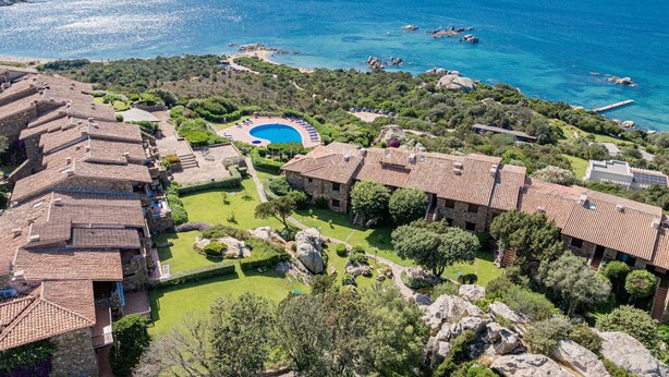A resort with terracotta-roofed villas, a central swimming pool, and a view of the sea.