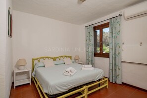 A bedroom with a bed, two bedside tables, a window with curtains, and an air conditioning unit.
