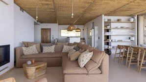 A living room with a sectional sofa, a coffee table, a TV, and a dining area with chairs and a table.