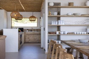 Een moderne keuken met houten kastjes, een eethoek met een houten tafel en stoelen, en een groot raam dat zorgt voor natuurlijk licht.