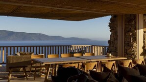 An outdoor seating area with a table and chairs, a stone wall, and a view of the sea.