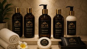 A bathroom vanity with five bottles of SAAR Palampur Villa products, a vanity kit, and a rolled towel with a flower.