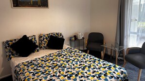 A hotel room with a bed, two chairs, a small table, a painting on the wall, and a window with curtains.