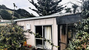 A small, single-story building with a large sliding glass door, surrounded by lush greenery and a mountain backdrop.