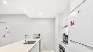 A modern kitchen with white cabinetry, a stainless steel sink, a built-in oven, and a refrigerator.