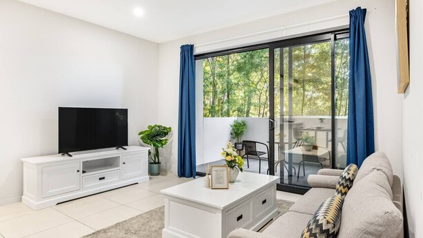 A modern living room with a flat-screen TV, white console, and a sofa.