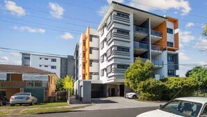 A modern multi-story residential building with balconies, a garage, and a parking area.