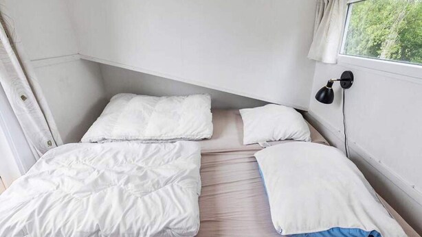 A small, single-bed room with a window and a wall-mounted lamp. - 4 Person Holiday Park Home in Vipperod (Vipperod)