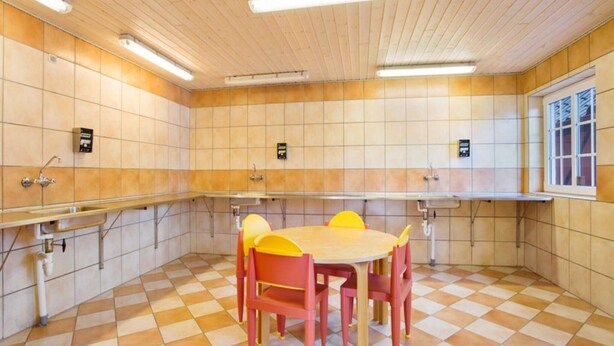 Eine öffentliche Toilette mit Schachbrettfußboden, Holzwänden und einem Fenster rechts.