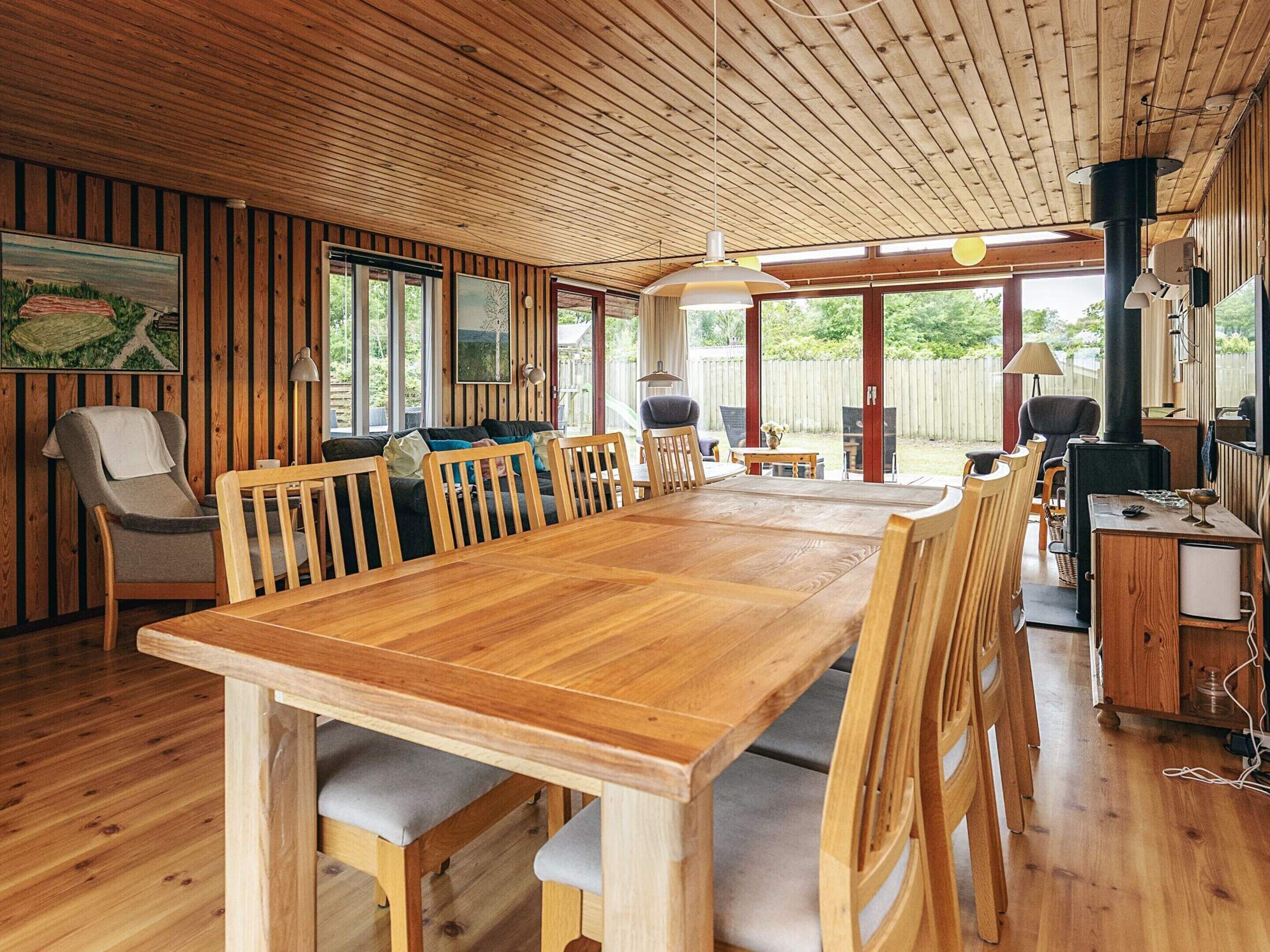 A spacious wooden dining area with a long table and multiple chairs, large windows, and a view of the outdoors.