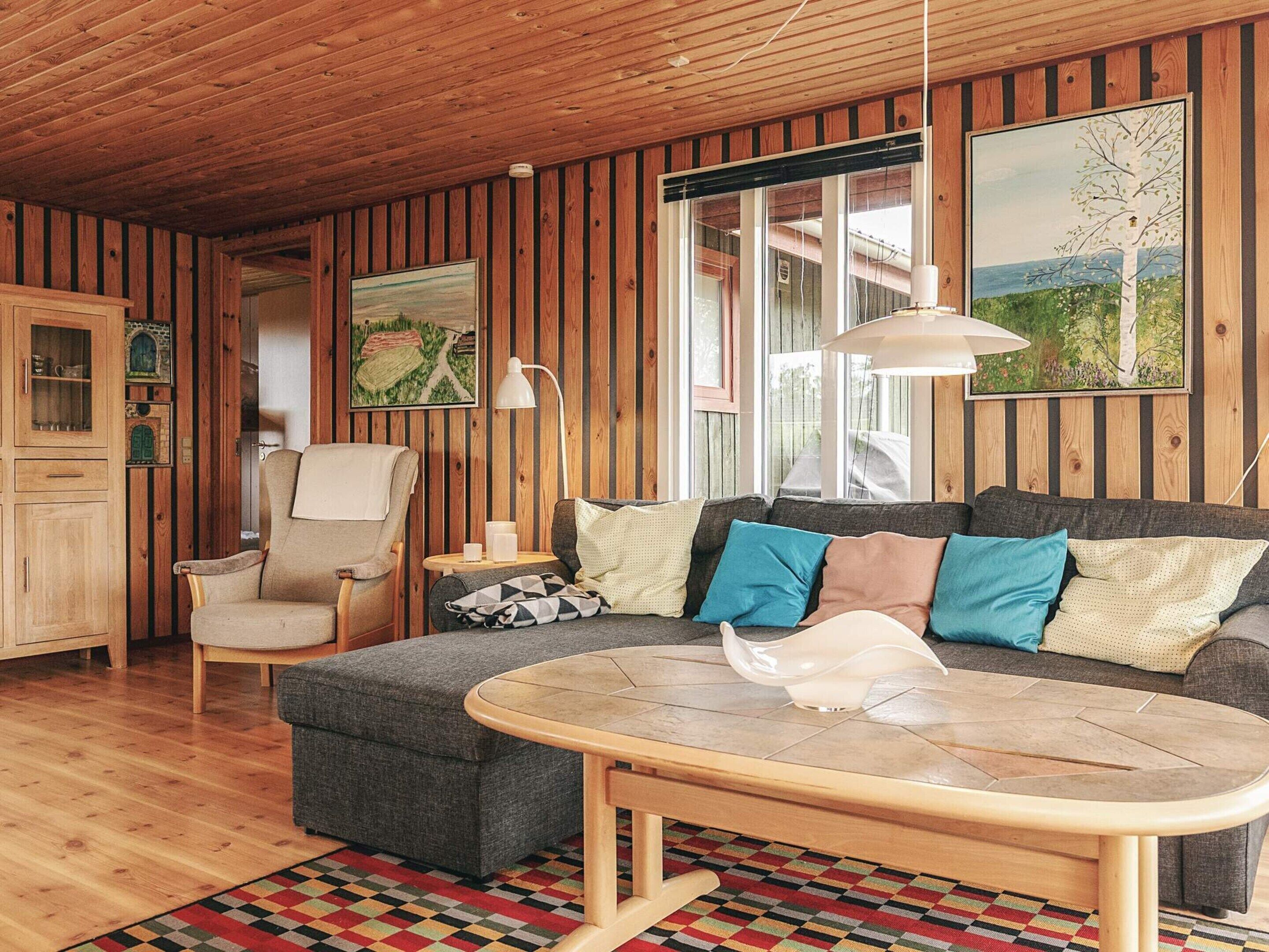 A cozy living room with wooden walls, a sofa with cushions, a chair, a small table, and a colorful rug.