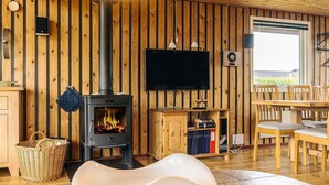 A cozy living room with a wood-paneled wall, a modern fireplace, a flat-screen TV, and a dining area with wooden furniture. - 4 Star Holiday Home in Hadsund (Hadsund)