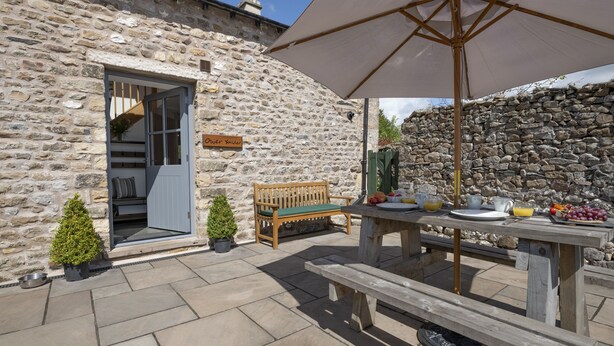 Un bâtiment en pierre avec un banc en bois et une table de pique-nique, une petite plante en pot et une pancarte indiquant « Oberlander ».