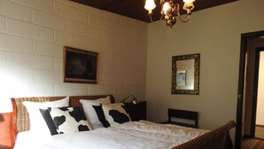 A bed with a white bedspread and black and white pillows, a wicker headboard, a wall-mounted mirror, and a chandelier. - 2 Person Holiday Park Home in Tranekaer (Tranekaer)