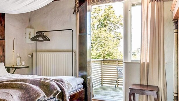 A bedroom with a bed, a bedside table, a lamp, a window with curtains, and a view of the outdoors. - 2 Person Holiday Park Home in Bastad (Bastad)