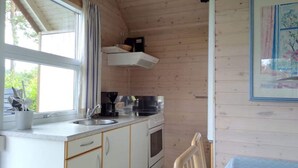 A compact kitchen with wooden walls, a window, a sink, a stove, and a chair. - 6 Person Holiday Park Home in Skagen (Skagen)