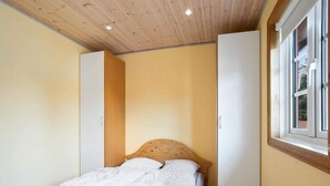 A bedroom with a wooden ceiling, a bed with white bedding, a window, and a wardrobe.