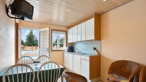 A compact kitchen with white cabinets, a dining table with chairs, and a wicker sofa.