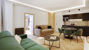 A modern living room with a green sofa, a beige sofa, and a dining area with a round table and chairs. - The Upper Marais Superb Apartment for 6 People (Paris)