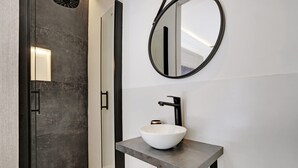 A modern bathroom with a white vessel sink, a round mirror, and a glass shower enclosure. - The Upper Marais Superb Apartment for 6 People (Paris)