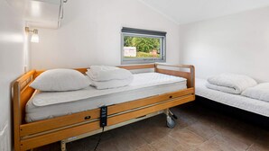 Een eenpersoonskamer met een houten bed, een klein raam met uitzicht, een nachtkastje en een wandlamp.