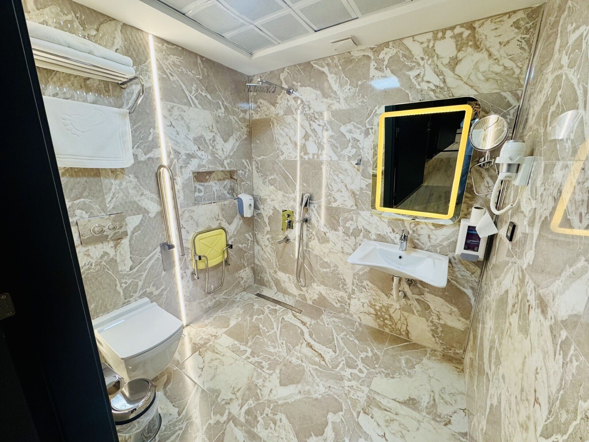 Een badkamer met een marmeren vloer, een wit wastafelmeubel, een spiegel en een douche.