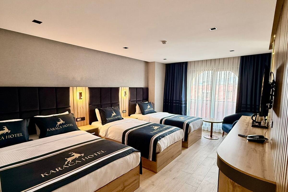 Habitación de hotel con tres camas, un escritorio y vistas a la ciudad.