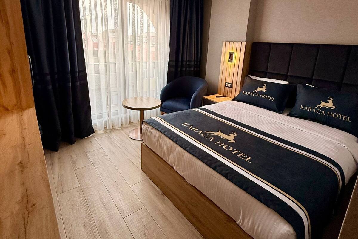 Habitación de hotel moderna con una cama grande, una mesita redonda y vistas de la ciudad a través de cortinas traslúcidas.