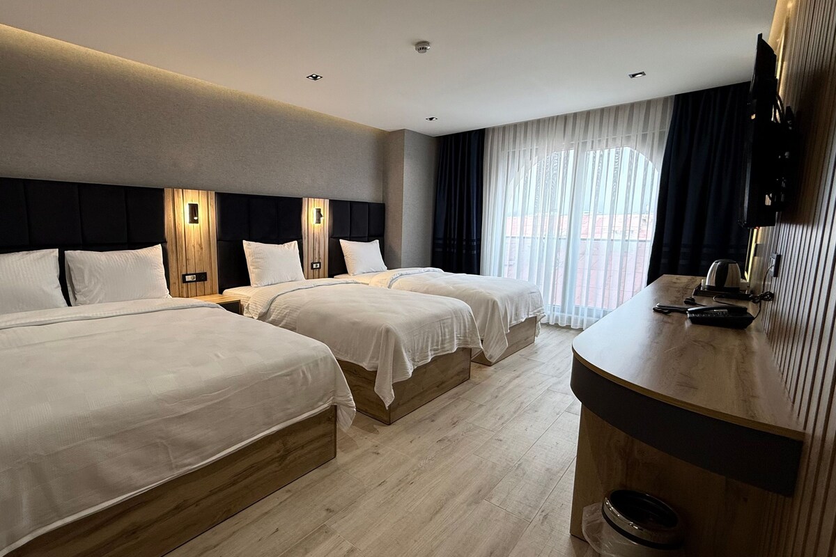 A hotel room with two beds, a wooden headboard, a flat-screen TV, and a large window with curtains.