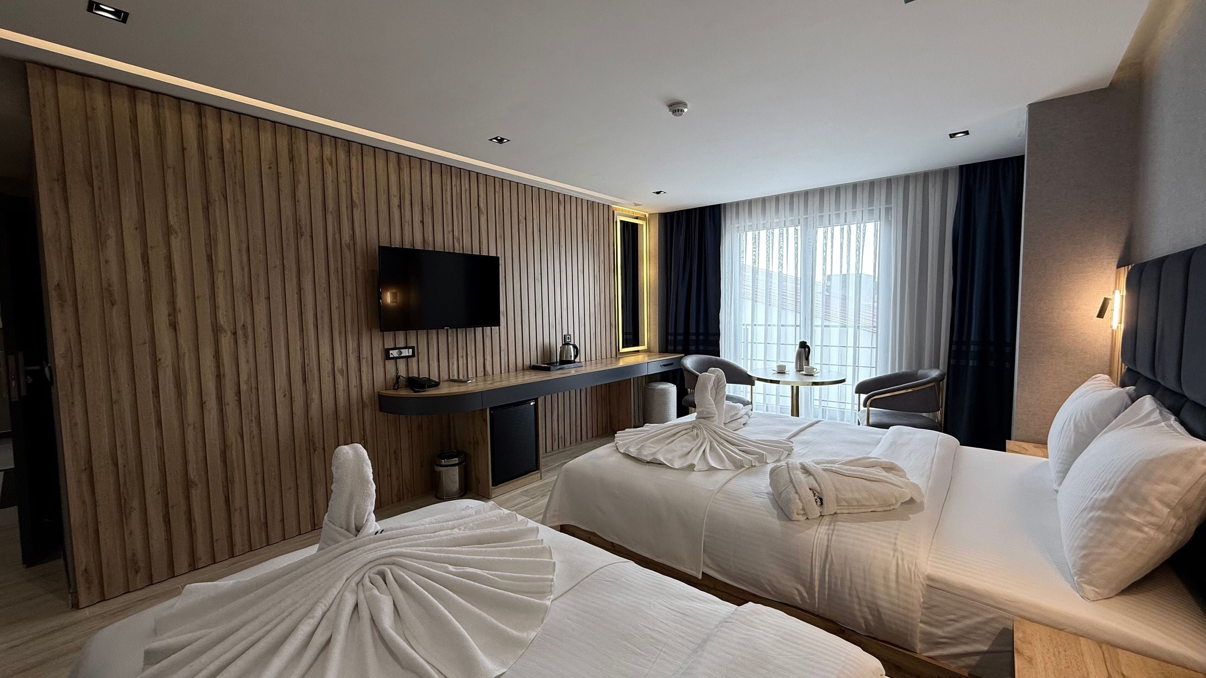 A hotel room with two beds, a TV, a desk, and a window with curtains.