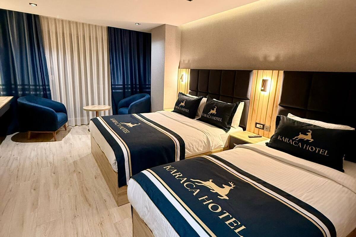 Habitación de hotel con dos camas, cada una con cabecera y almohada con el logotipo del hotel. También hay una mesita redonda y una silla azul en la habitación.