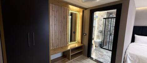 A modern bedroom with a wooden wardrobe, a bench, a large mirror, and a glass shower enclosure.