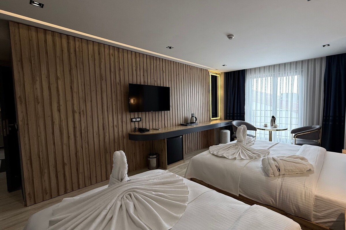 Ein Hotelzimmer mit zwei Betten, einem Fernseher, einem Schreibtisch und einem Fenster mit Vorhängen.