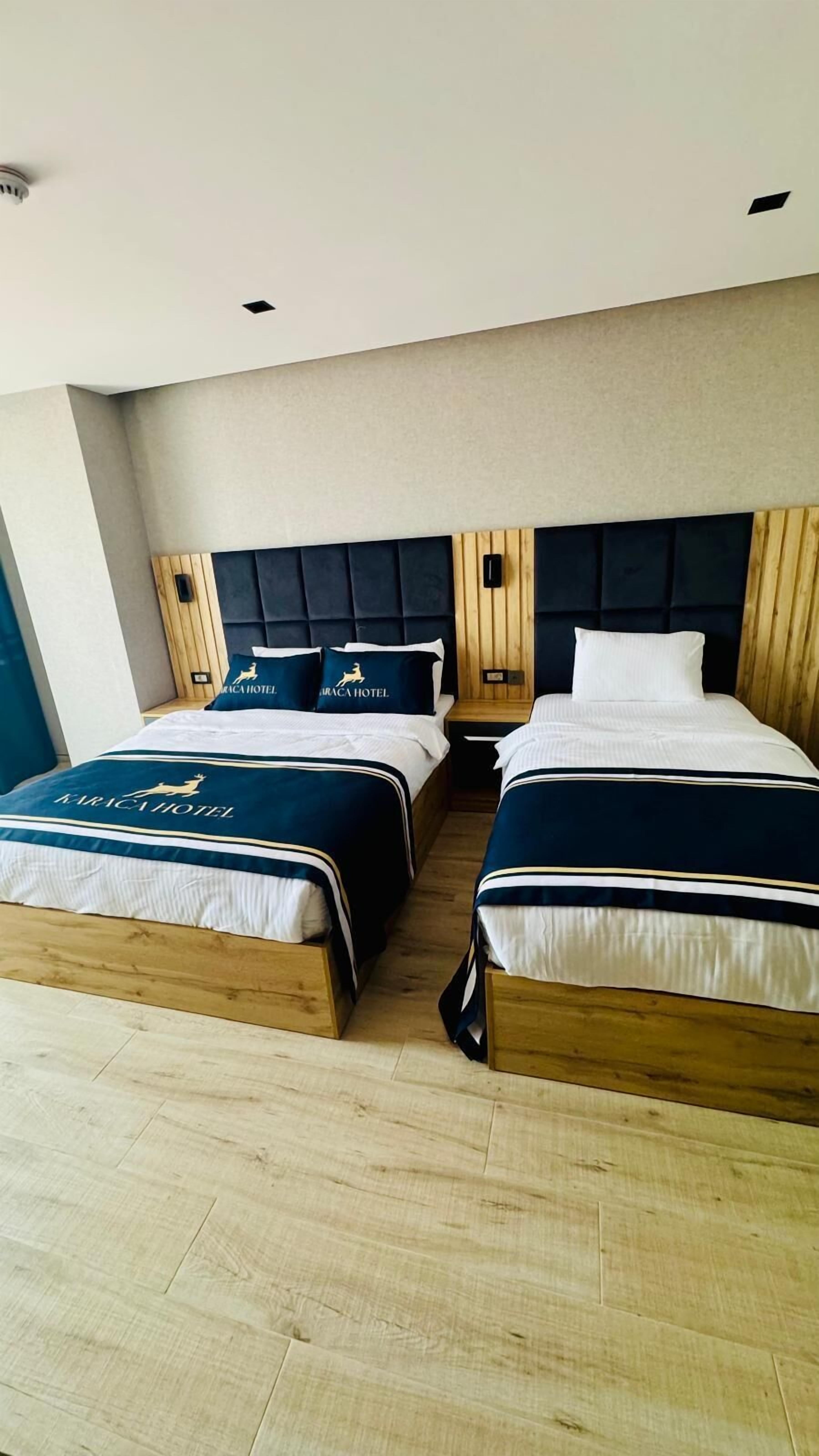 Habitación de hotel con dos camas, cada una con cabecero de madera y colcha azul oscuro.