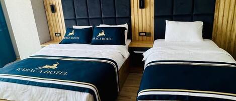 Habitación de hotel con dos camas, cada una con cabecero de madera y colcha azul oscuro.