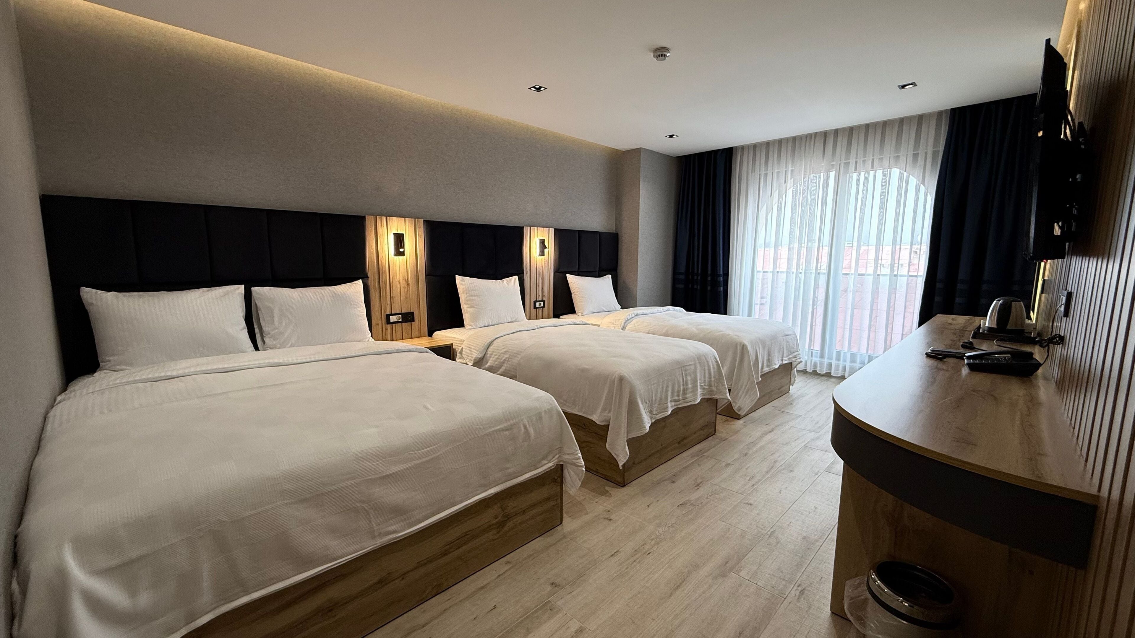 A hotel room with two beds, a wooden headboard, a flat-screen TV, and a large window with curtains.