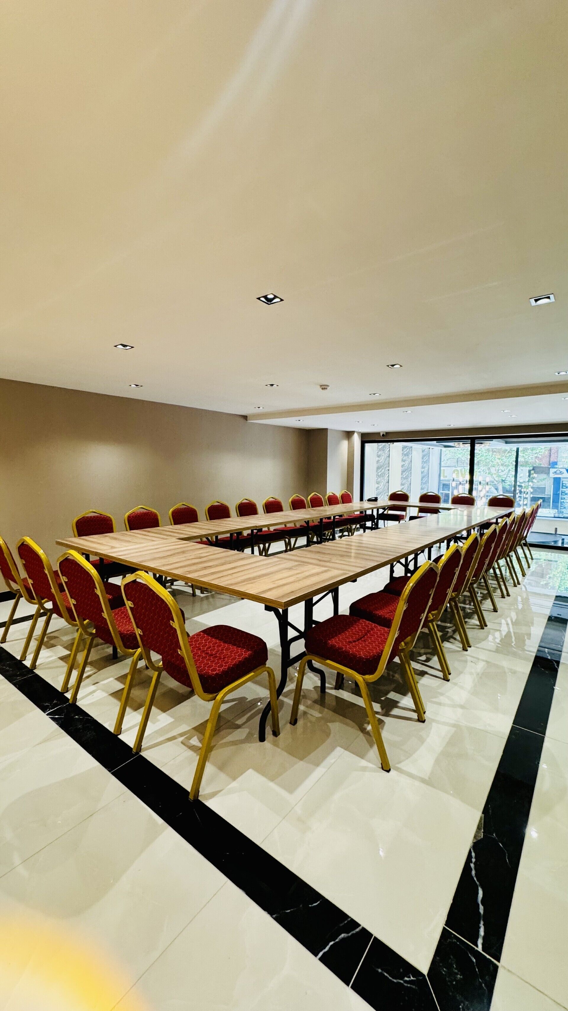 Una sala de conferències amb una taula llarga i cadires vermelles, finestres grans i un paviment de rajoles.