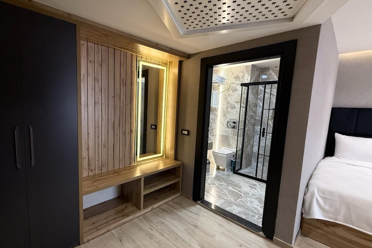 A modern bedroom with a wooden wardrobe, a bench, a large mirror, and a glass shower enclosure.