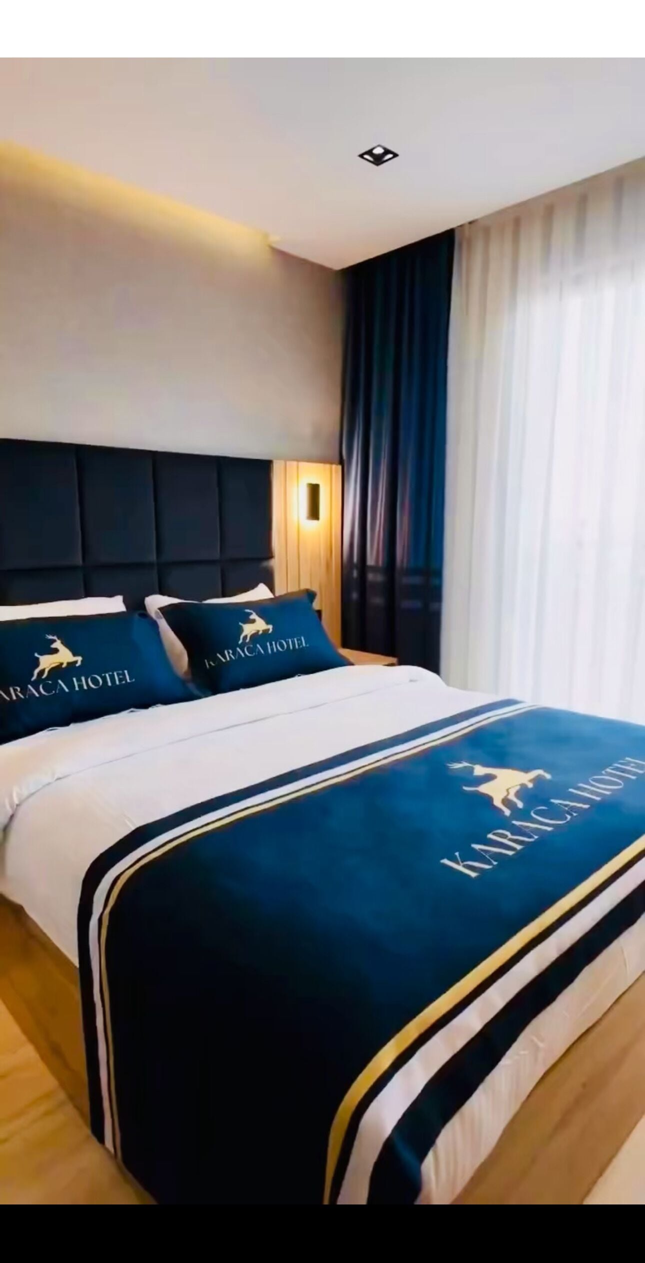 A hotel room with a large bed, dark headboard, and a view of the city through the window.