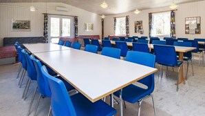 Un salón de conferencias con una larga mesa y sillas azules, paredes blancas e iluminación en el techo.