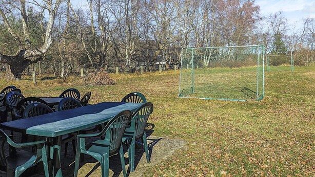 Un espacio al aire libre cubierto de césped, con un arco de fútbol, una mesa y sillas, y hojas en el suelo.
