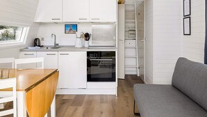 A compact kitchen with white cabinets, a dining area with a wooden table, and a grey sofa. - 6 Person Holiday Park Home in Bogense (Bogense)