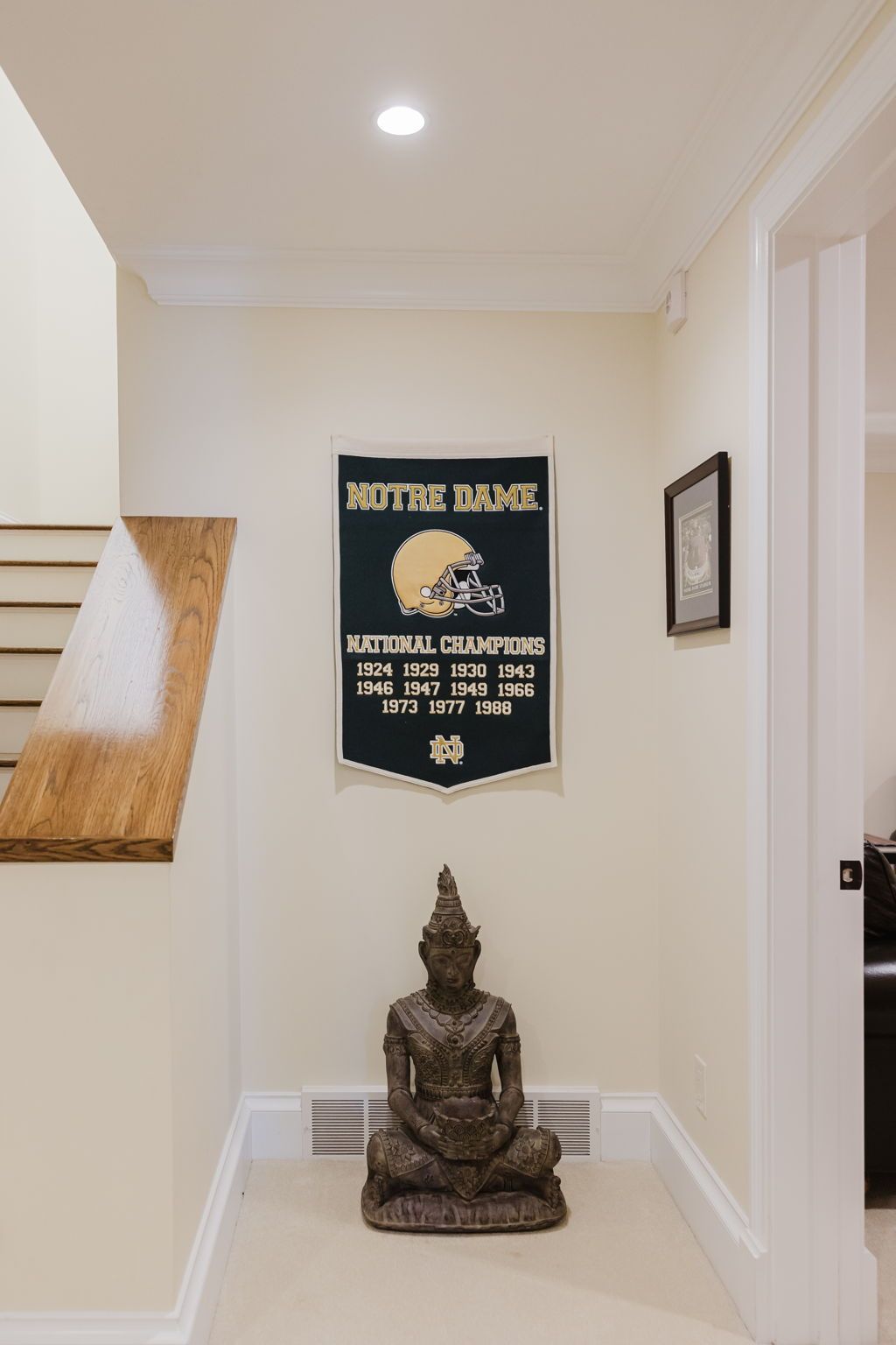 Un couloir orné d’une plaque commémorative encadrée célébrant les victoires de l’équipe de Notre Dame, d’une statue et d’un mur fait de lattes de bois.