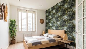 A bedroom with a wooden bed, a window, a potted plant, a woven wall hanging, and a textured wall. - DIFY Paul Bert - Part-dieu (Lyon)