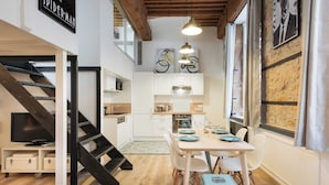 A modern kitchen with white cabinets, a dining table with blue plates, and a staircase with black railings.