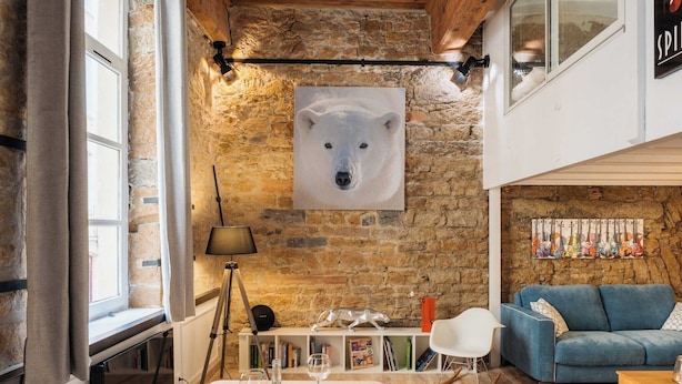 A cozy room with a stone wall, a polar bear artwork, a blue sofa, and a dining area with a table set for two.
