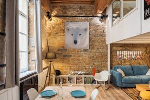 Ein gemütliches Zimmer mit Steinwand, einem Polarbär-Kunstwerk, einem blauen Sofa und einem Essbereich mit Tisch für zwei Personen.