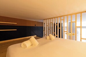 Une chambre d’hôtel avec un lit, une tête de lit en bois, une fenêtre donnant sur un paysage agréable et un luminaire suspendu.