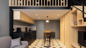 Ein gemütlicher Wohnbereich mit Küchenzeile, einem grauen Sofa, einem Holztisch und einem Fernseher auf einem Holzgestell.